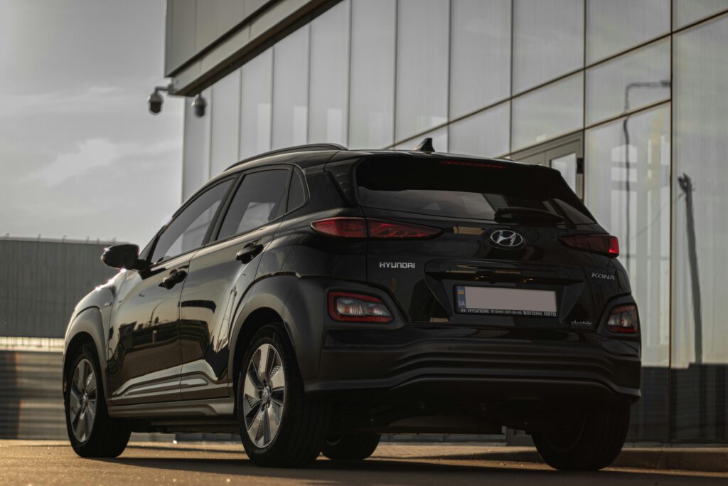 pexels photo 17534546 17534546 Rear view of a black Hyundai Kona parked next to a contemporary glass building reflecting urban architecture.